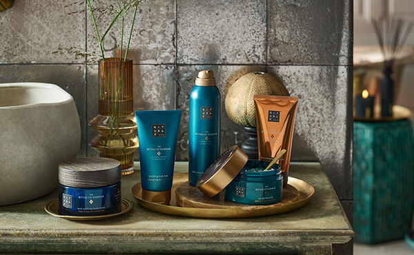 Essentiels de soin The Ritual of Hammam disposés sur une étagère de salle de bain avec d’autres objets en cuivre pour une expérience spa à la maison.